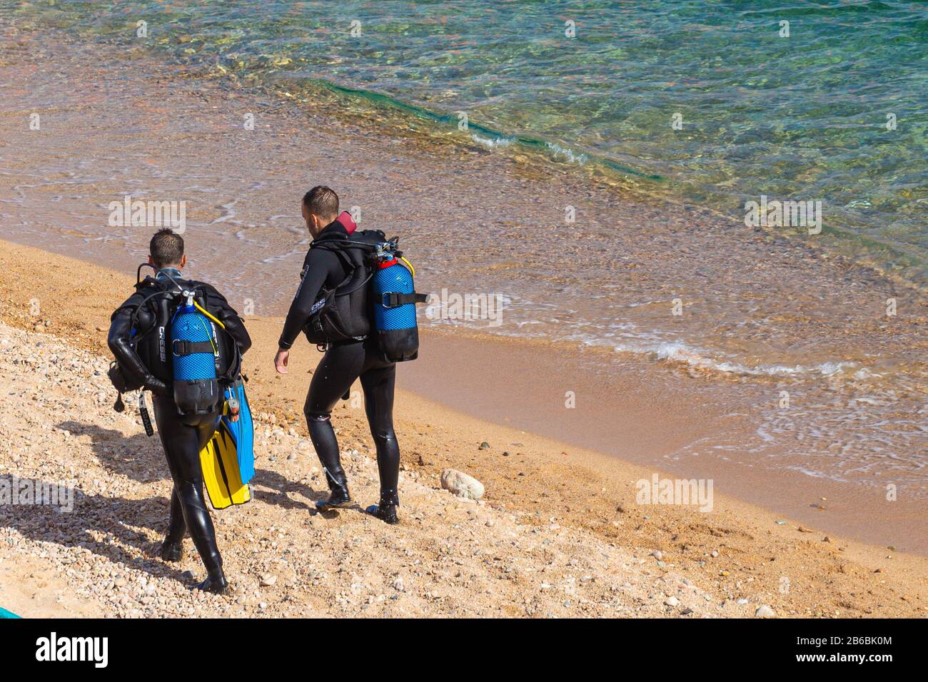 TOSSA DE MAR,SPAIN - AUGUST 4, 2019: Two unknown divers in wetsuits and scuba divers on a sandy beach near the water's edge are preparing for a dive Stock Photo