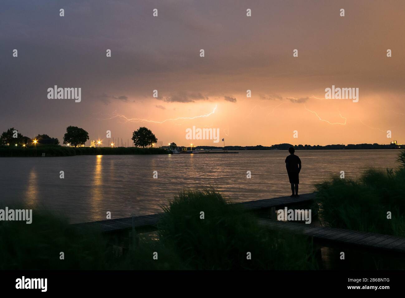 Silhouette of a boy who is watching a lightning storm over a lake in The Netherlands Stock Photo