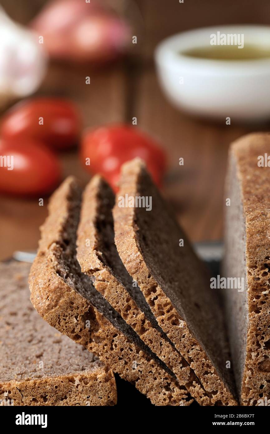 Gluten free buckwheat bread on a cutting board with tomatoes, onion and garlic on the background. Stock Photo