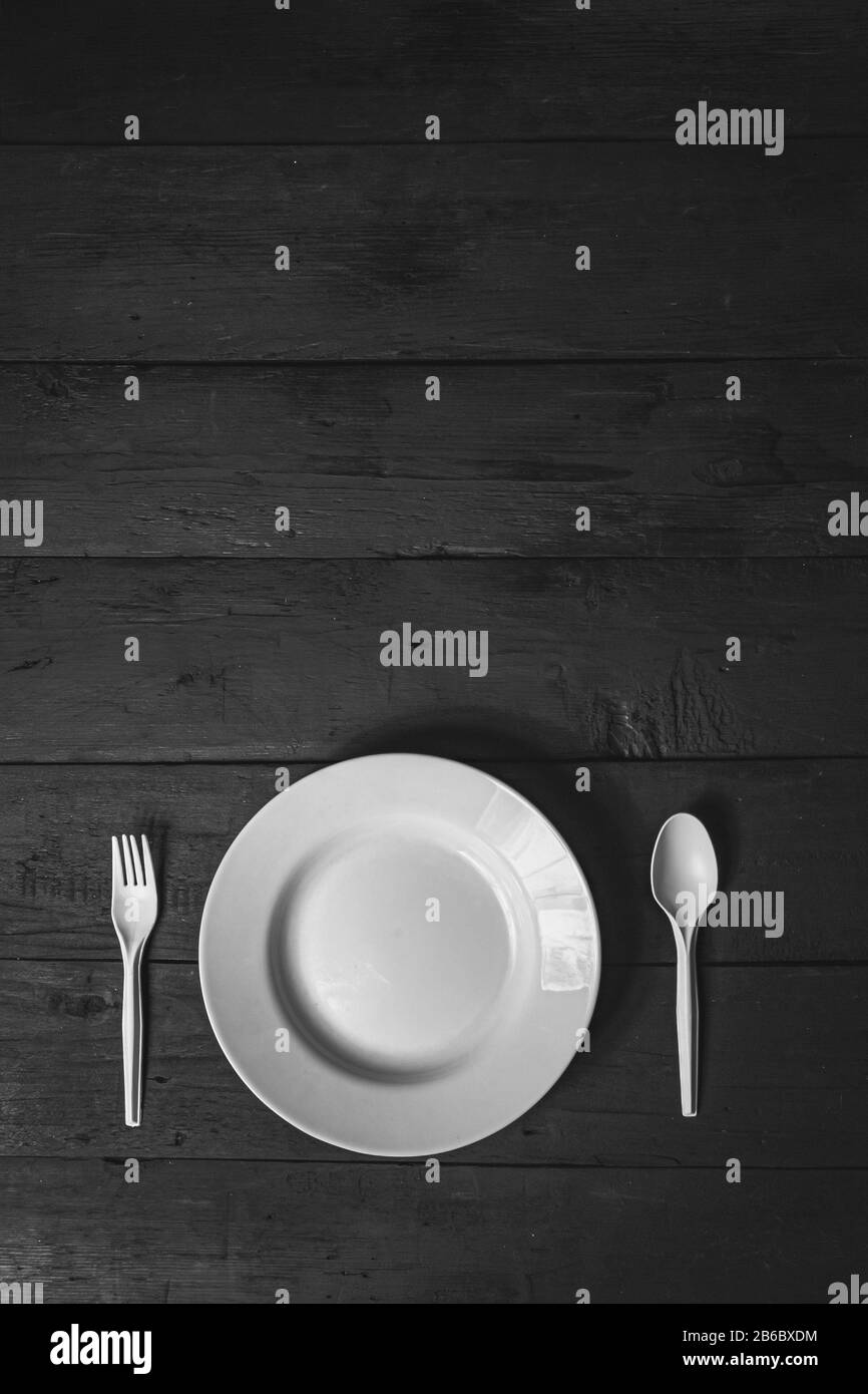 Empty white bowl, fork and spoon on black wood table, close-up view. Diet concept: flat lay of clean kitchen dishes on dark rustic background Stock Photo
