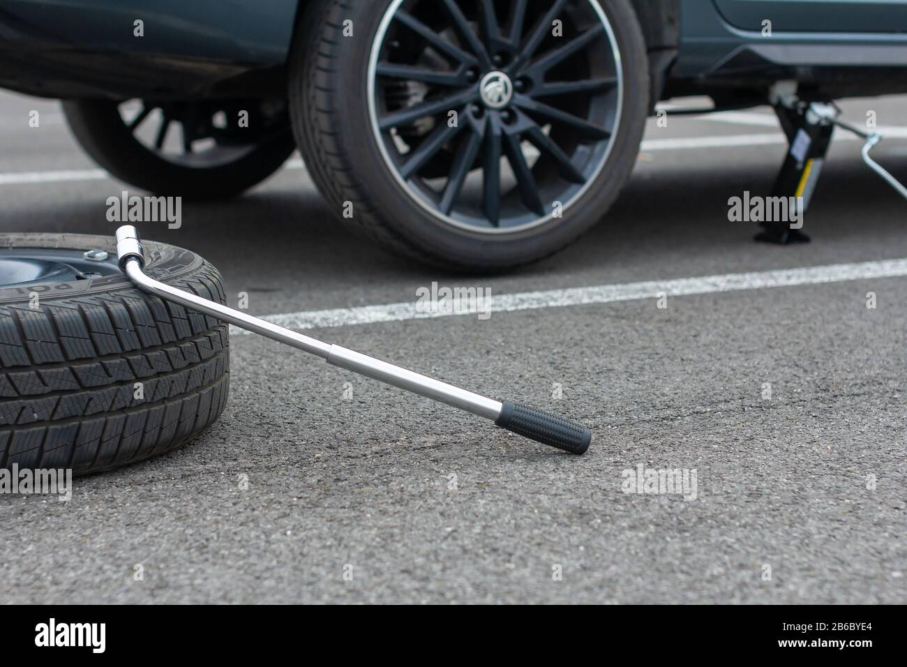 A flat tire car wheel and screwdriver are on a asphalt road on the broken Skoda Rapid background. Jack is lifting up a vehicle. Automobile service Stock Photo