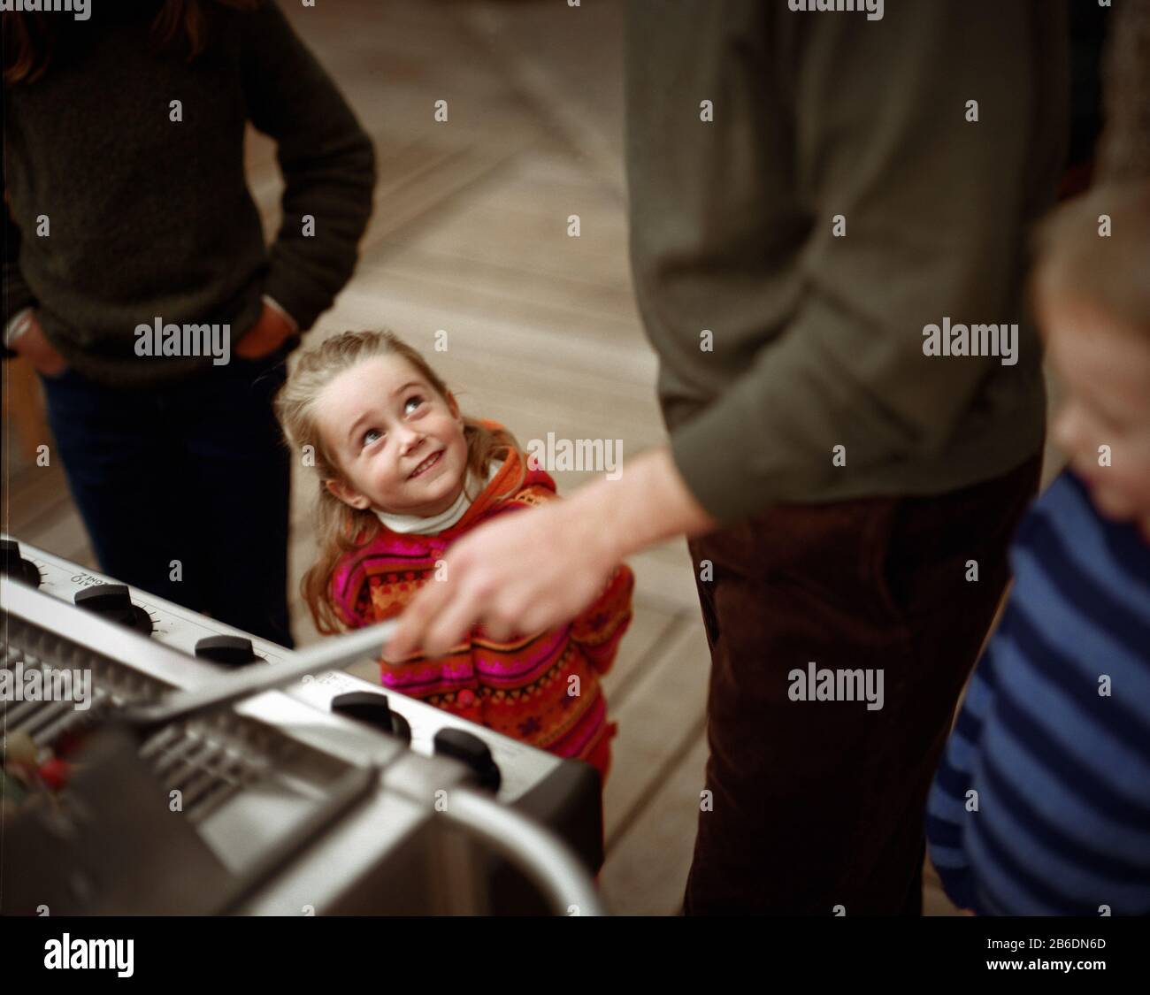 View of a small girl smiling while a man prepares barbecue. Stock Photo