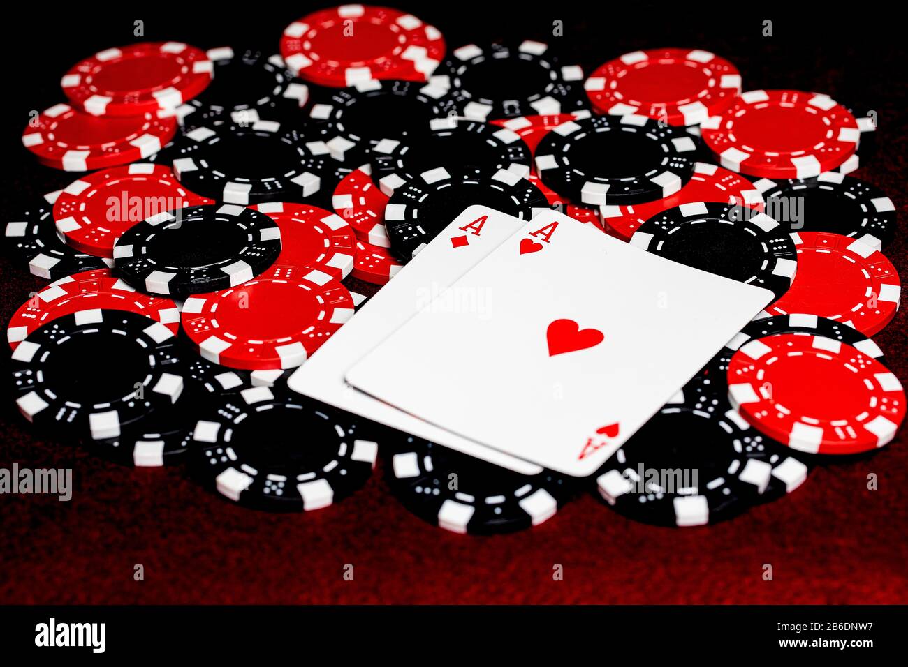 A pair of red aces, diamonds and hearts, on a pile or red and black clay poker chips.  Room for copy in the lower left of the image on the red felt ta Stock Photo