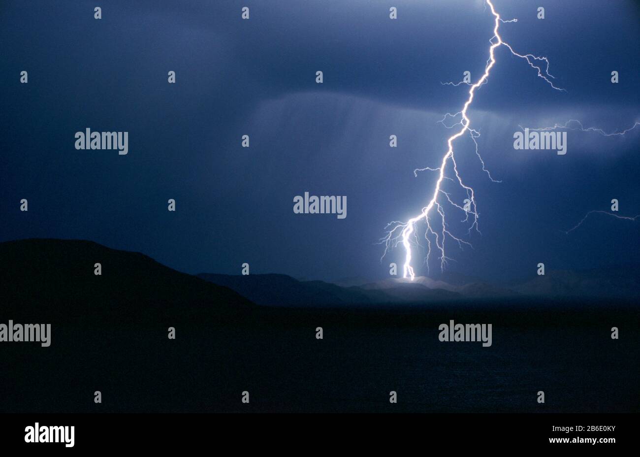 White lightning cracking across a moody dark sky at night. Stock Photo