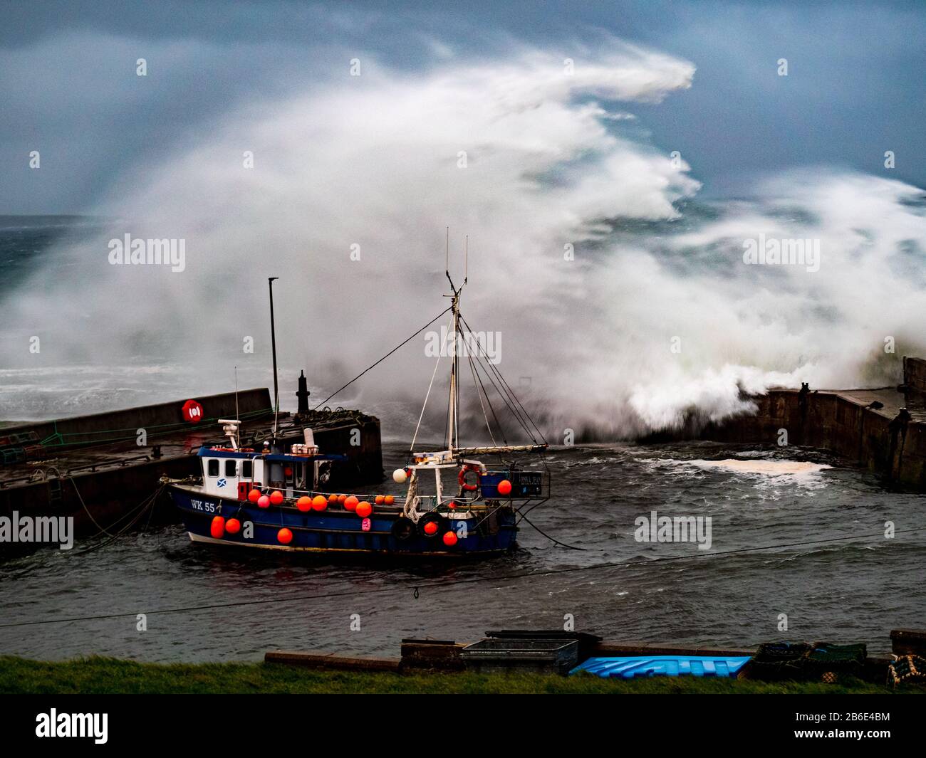 A wave crashes over the harbour wall protecting a fishing boat at John o'Groats, Highlands, Scotland, UK, Europe Stock Photo