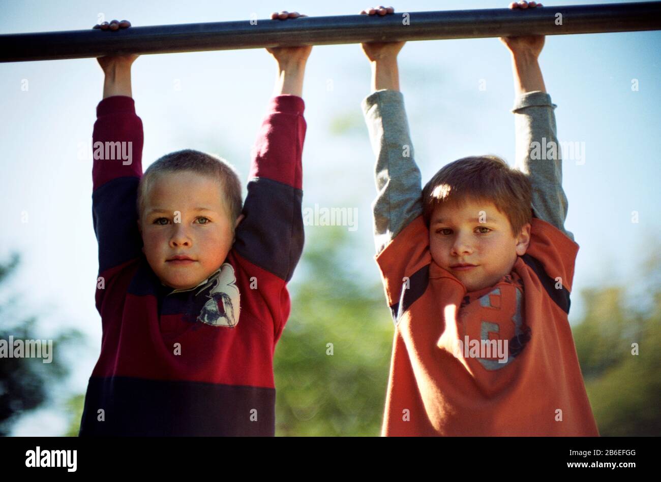 Two boys hanging on monkey bars Stock Photo