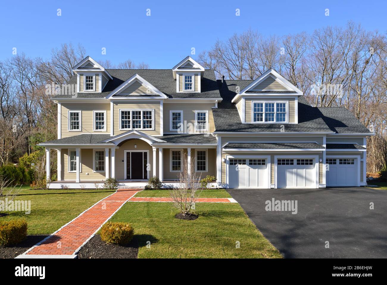 New house, colonial style, frontal view. Brick entrance walkway, paved driveway, landscaped garden. Stock Photo