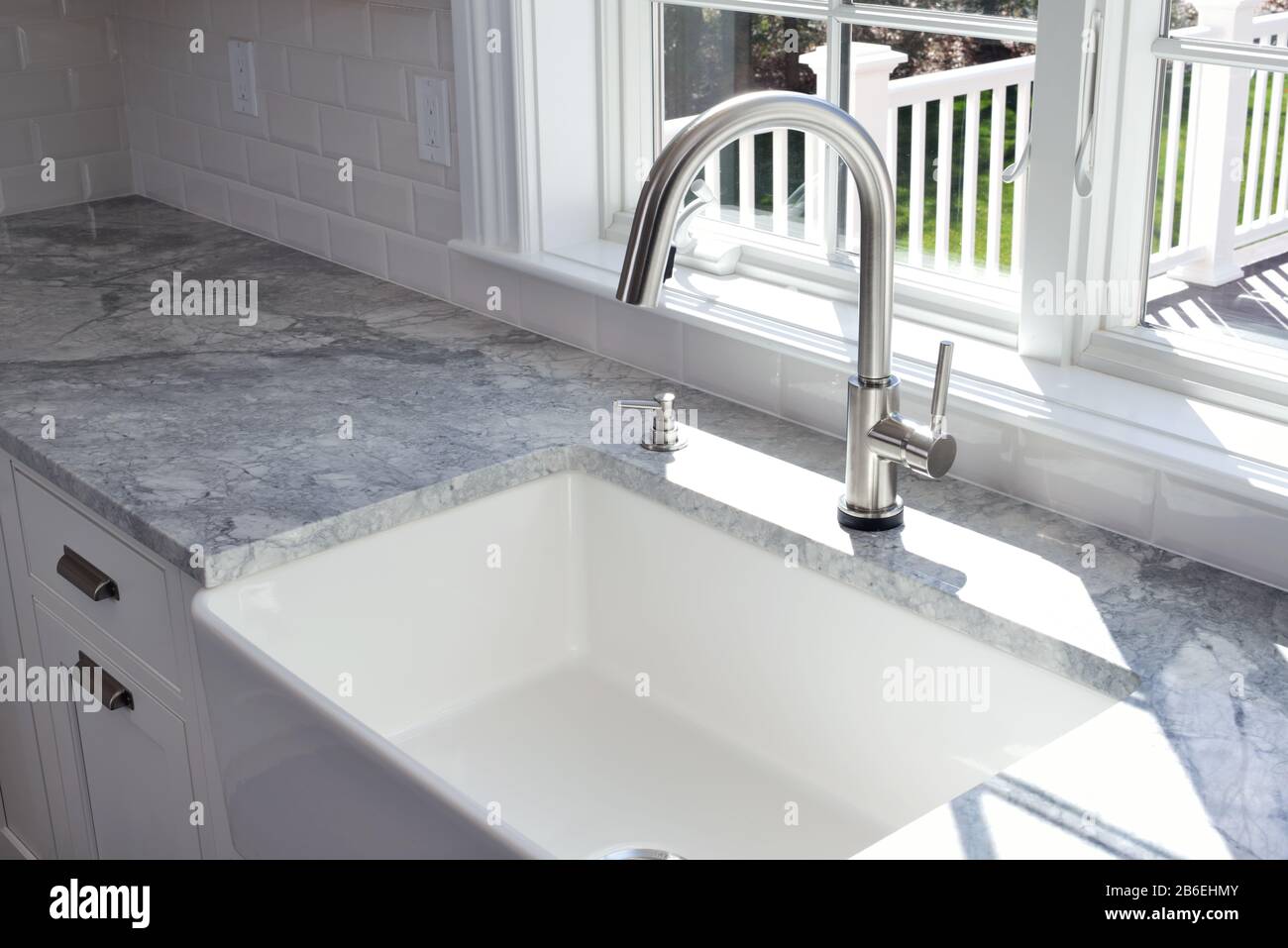 Modern kitchen sink and single handle brass faucet with soap dispenser, marble countertop and window to the garden. Stock Photo