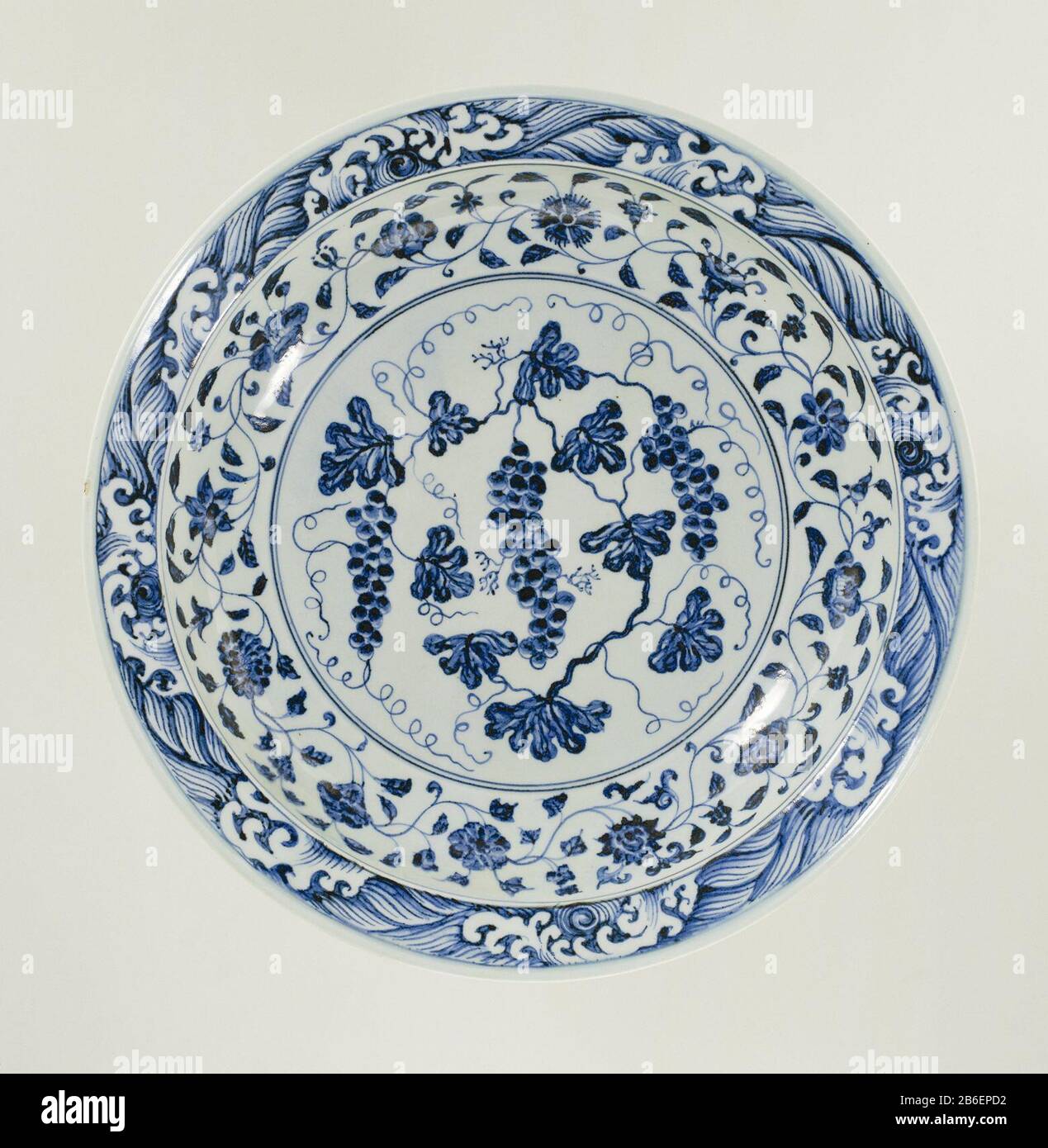 Dish plate with grapes and flower tendrils Schotel van porselein,  beschilderd in onderglazuur blauw. Op het plat een druivenrank. De wand met  een doorlopende bloemrank en de rand met een band met