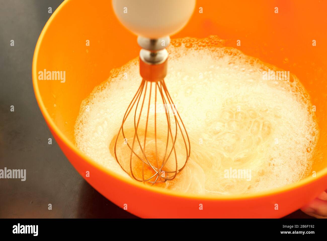 Mixing eggs in orange bowl with blender Stock Photo
