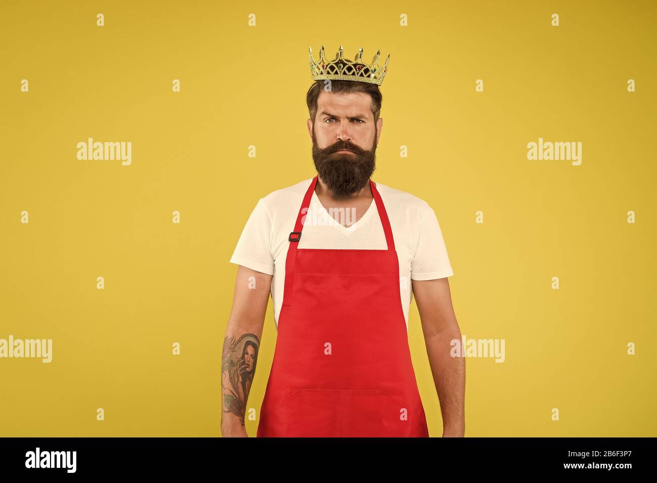 King of kitchen. Cook with beard and mustache yellow background. Man mature cook wear cooking apron and golden crown. Royal recipe. Ideas and tips. Chief cook and professional culinary. Cook food. Stock Photo