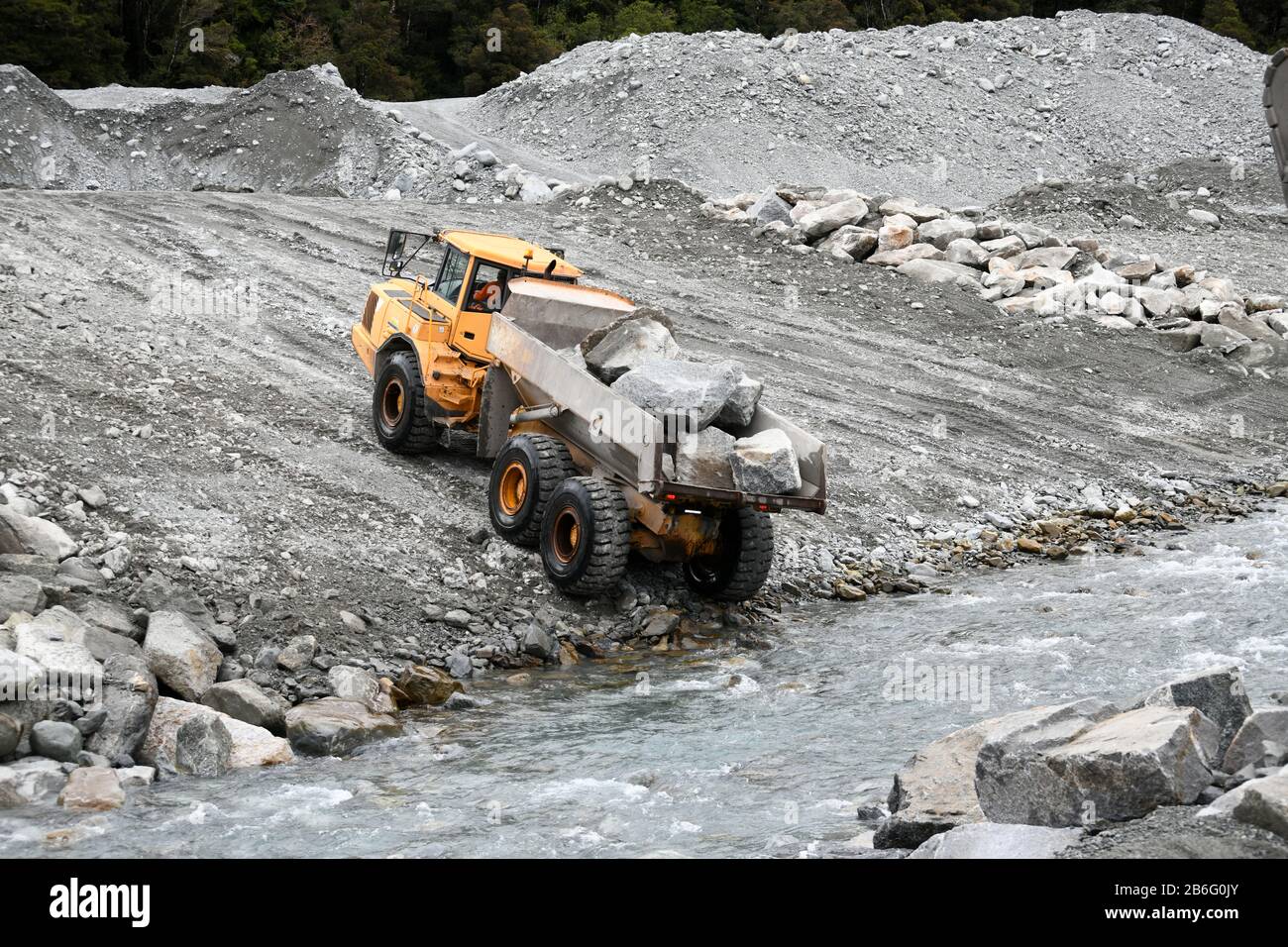 OTIRA, NEW ZEALAND, SEPTEMBER 19, 2019: A tip truck dumps a load of rock to create flood water control on a West Coast river just above a railway brid Stock Photo
