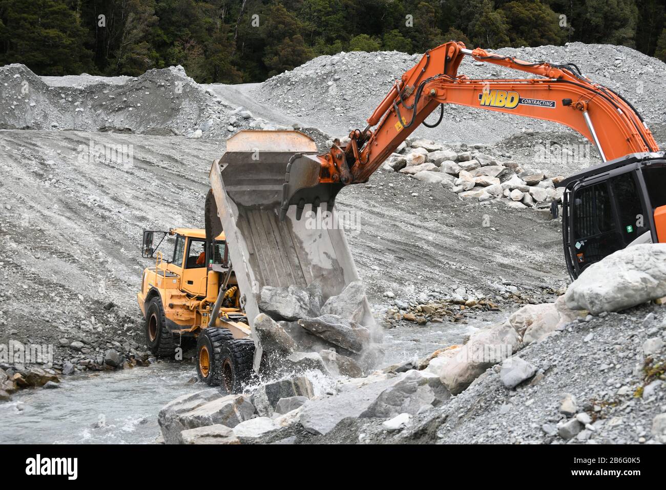 OTIRA, NEW ZEALAND, SEPTEMBER 19, 2019: A tip truck dumps a load of rock to create flood water control on a West Coast river just above a railway brid Stock Photo