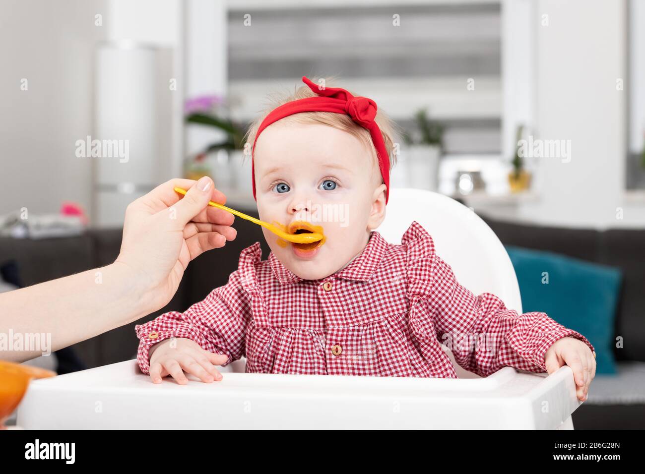 Mother Feeding Her Baby Daughter With Spoon - Mother Giving Healthy Food To Her Adorable Child At Home Stock Photo