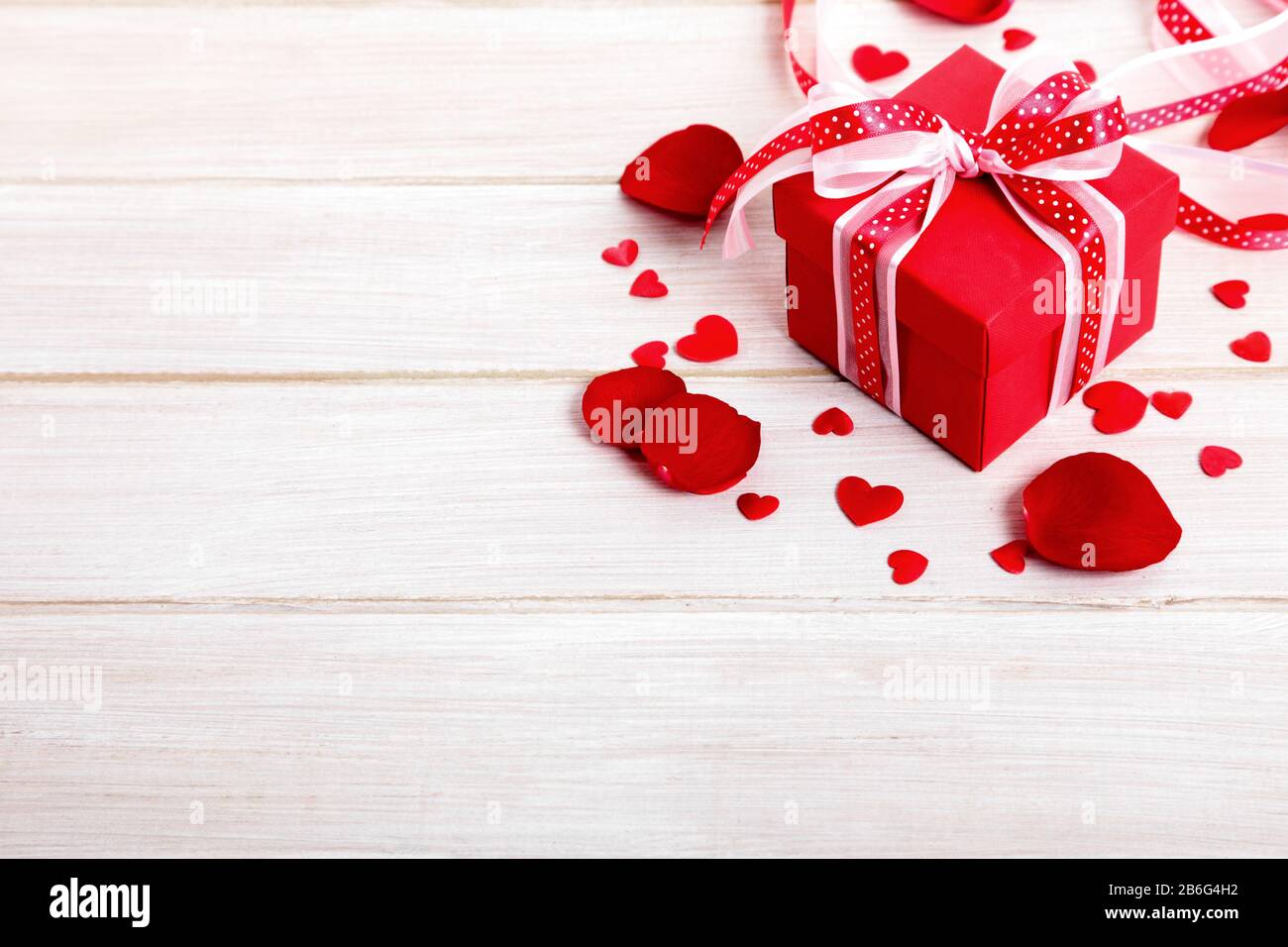 Valentine background of gift box and rose petals on white wood. Space for copy. Stock Photo
