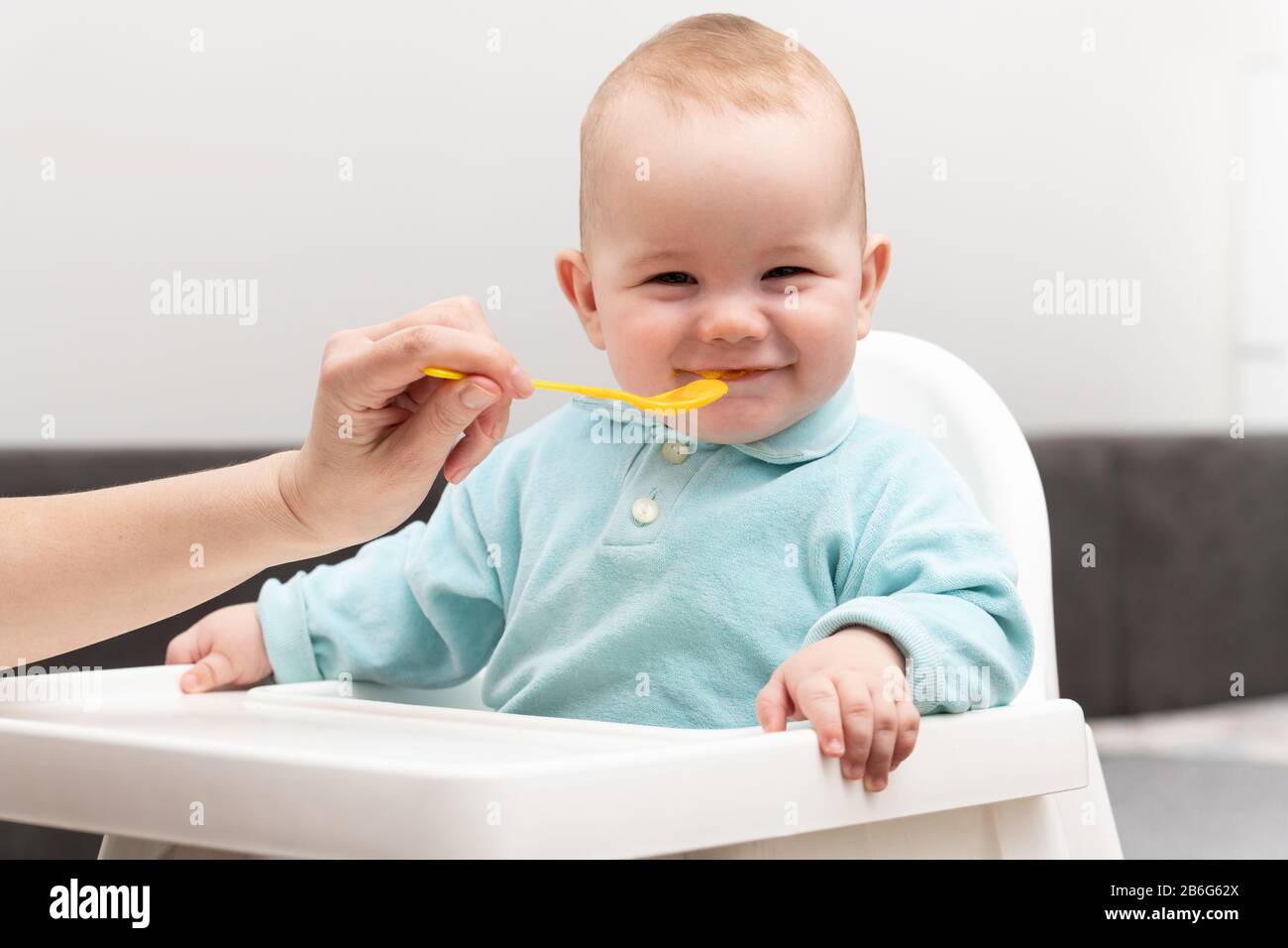 Mother Feeding Her Baby Son With Spoon - Mother Giving Healthy Food To Her Adorable Child At Home Stock Photo
