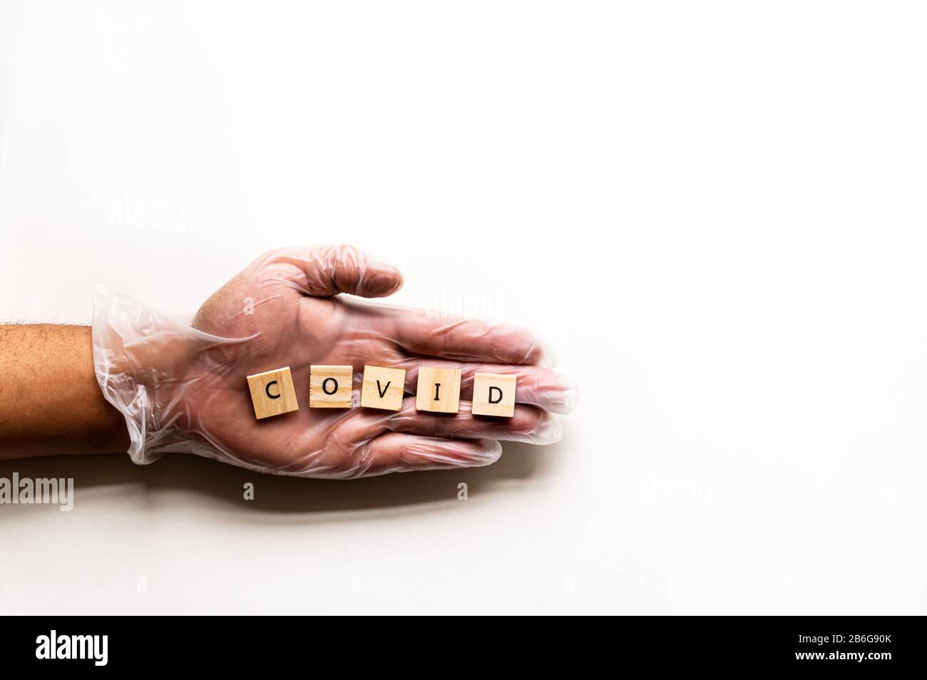 An isolated left hand wears a latex glove and displays the message 'COVID'. Stock Photo