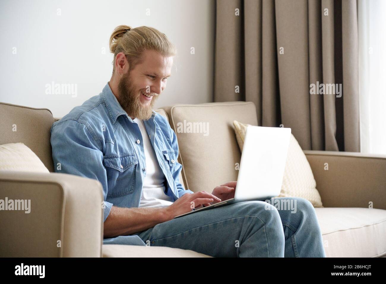 Young happy man modern laptop look at screen sit on sofa couch potato copyspace. Stock Photo