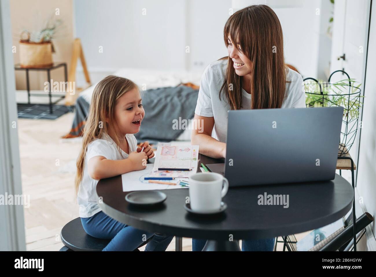 Working mom freelancer on the laptop with little daughter playing on the table together at home Stock Photo