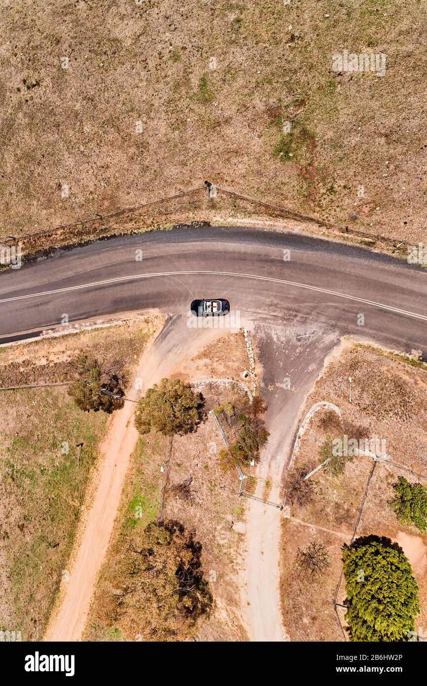 Driveway to rural remote farm in agriculture valley of Blue Mountains with small convertible passenger car passing by. Aerial top down view. Stock Photo