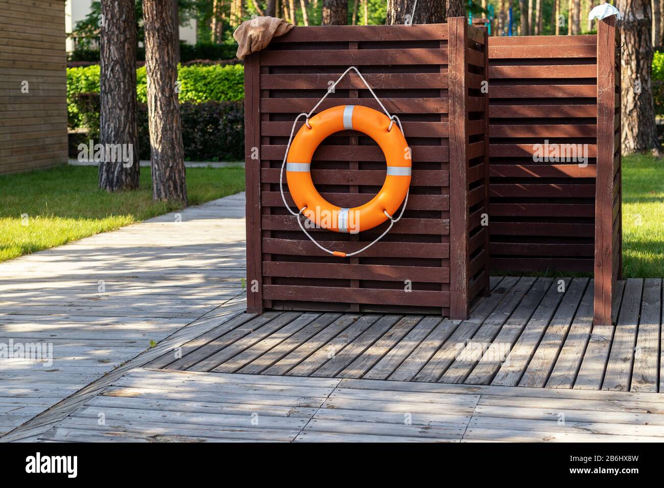Wooden dressing changing room with orange lifebuoy at recreation area near pond, pool or lake at forest eco-frinedly resort. Cabin on wood flooring Stock Photo