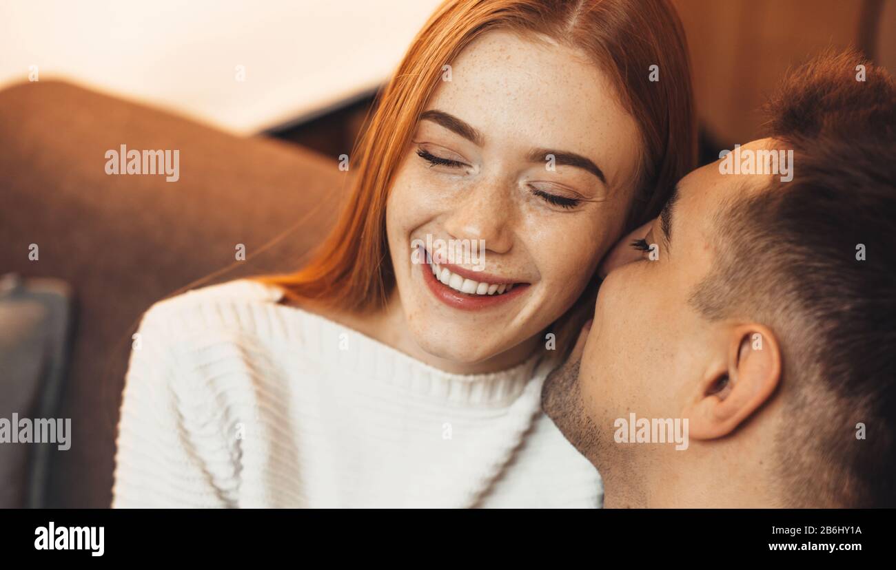 Ginger caucasian lady with freckles is cheering with her love while embracing on a sofa Stock Photo