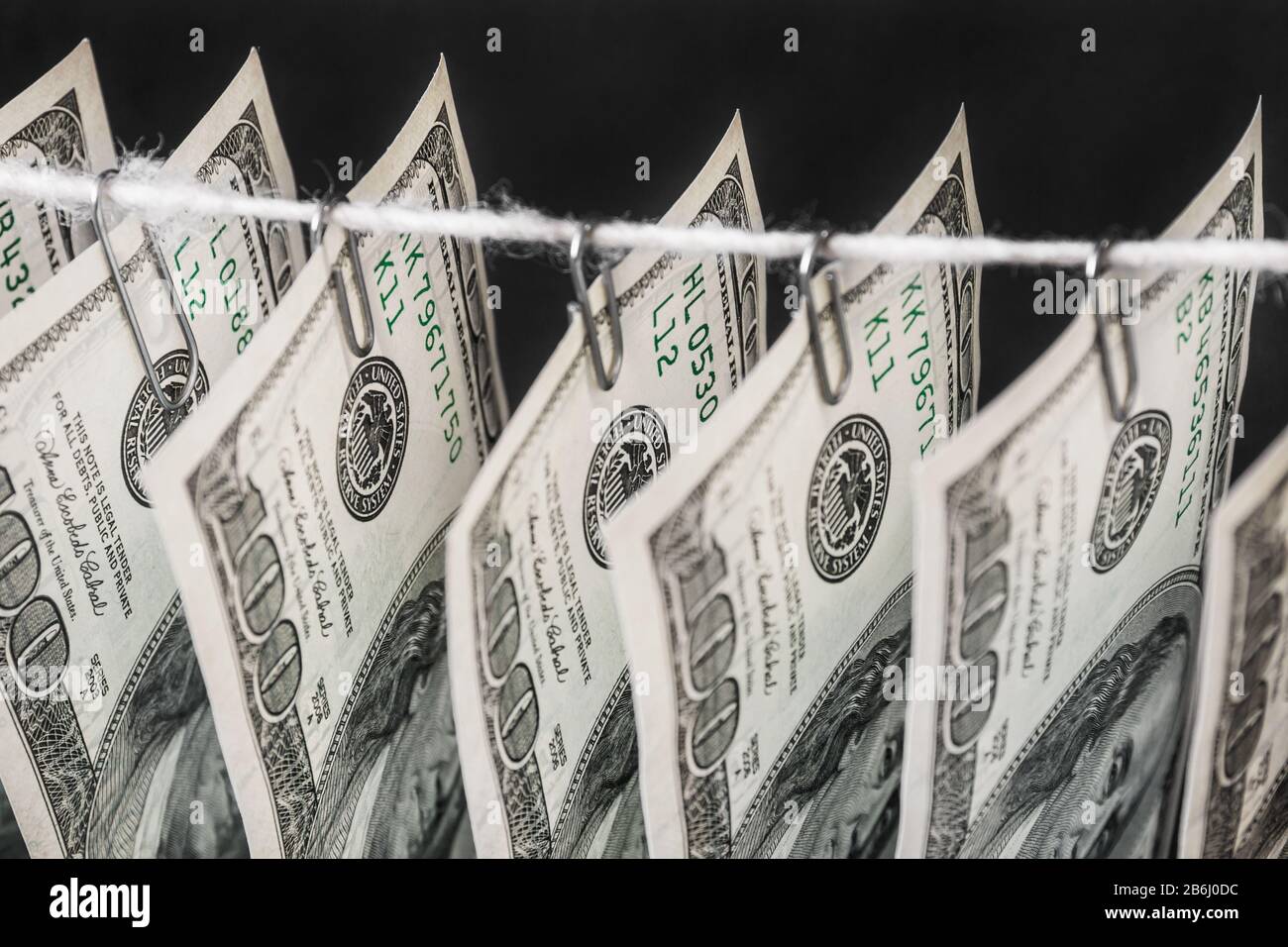 Parts of hundred dollar bills hanging on clerical clips on a rope on the dark background. Closeup, selective focus Stock Photo