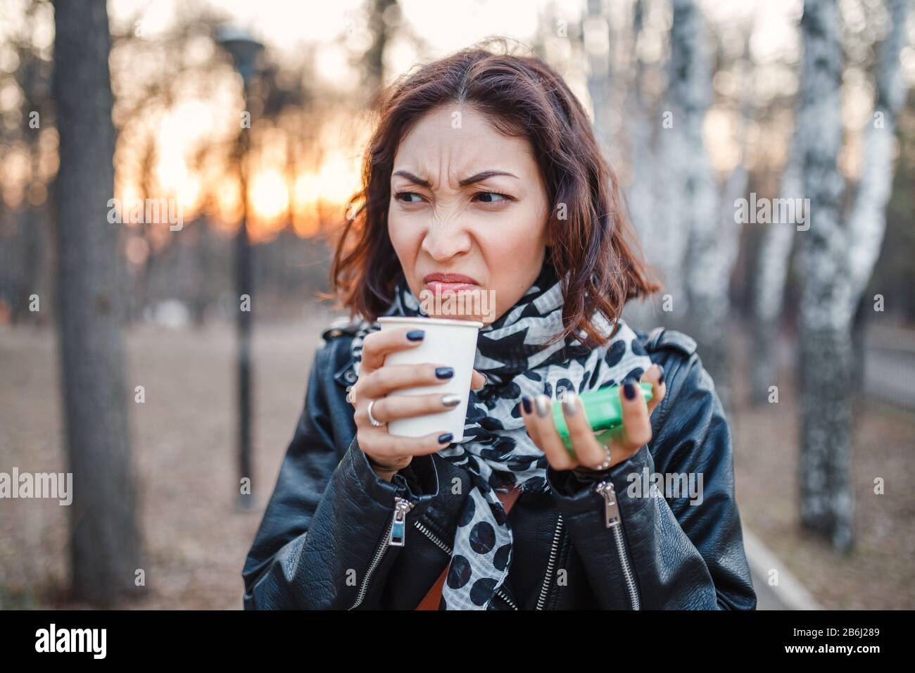 Shocked woman tries disgusting coffee or tea from a disposable takeaway coffee outdoors Stock Photo