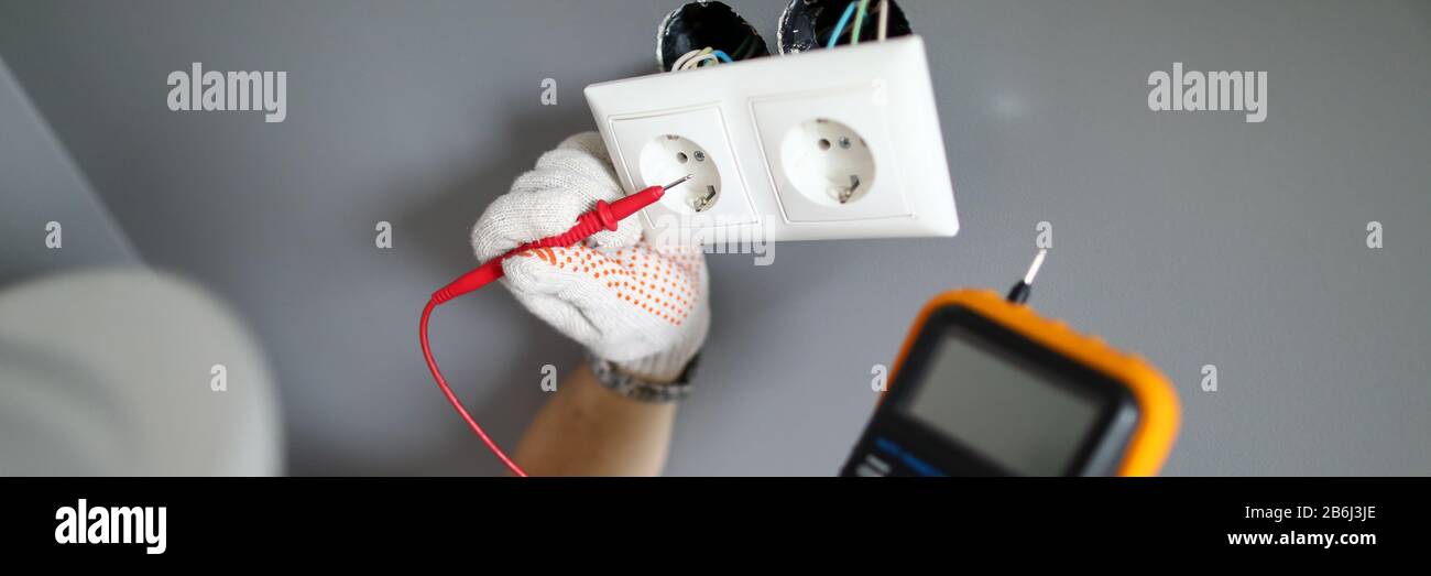 Repairman in gloves testing elecrticity and fixing socket with screwdriver Stock Photo