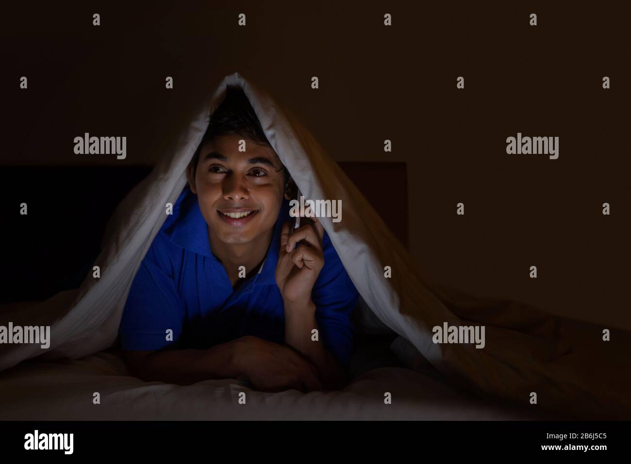 Teenage boy talking on his mobile phone in a dark room. Stock Photo