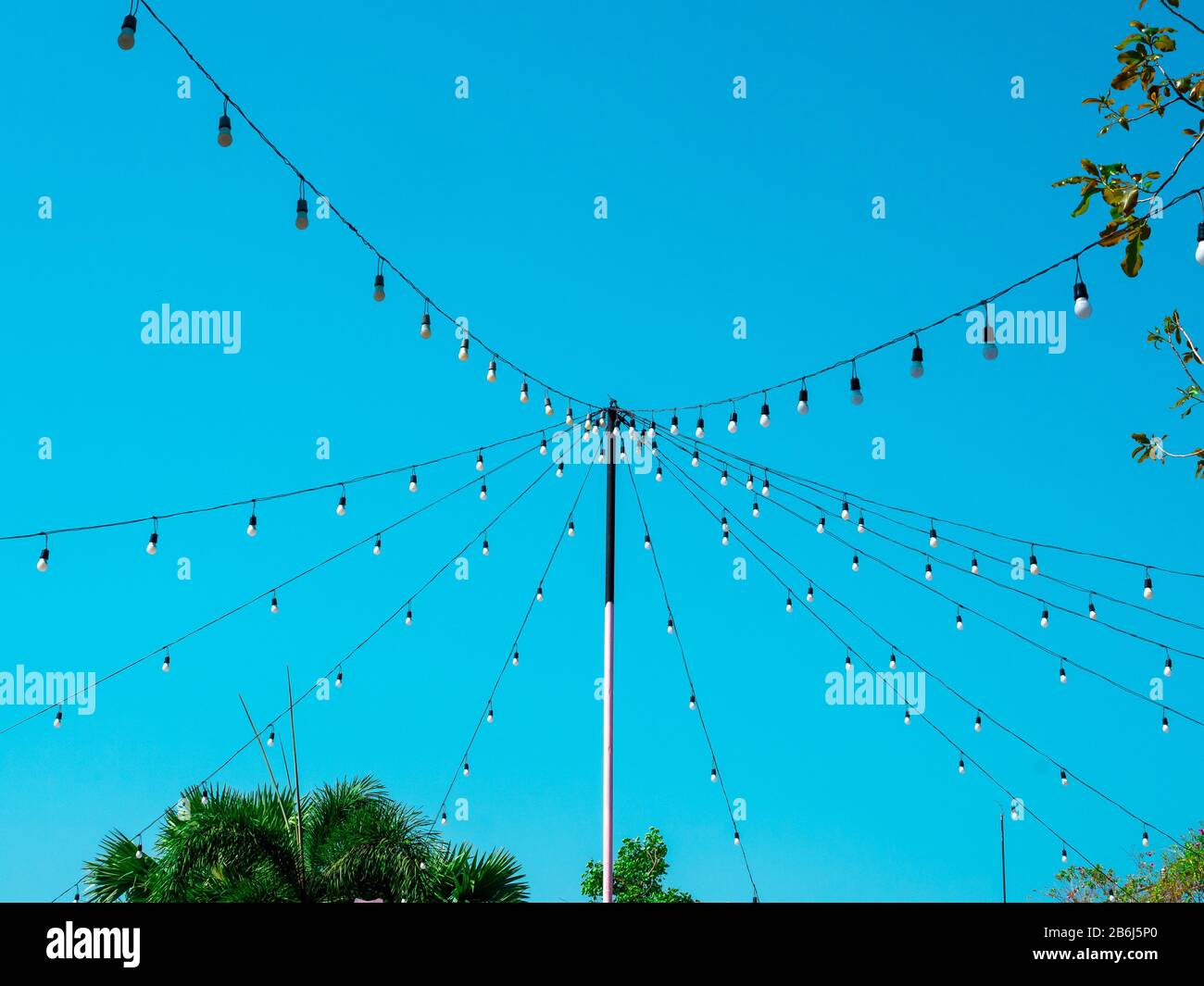String wired bulbs from the pole in outdoor garden on blue sky background. Stock Photo
