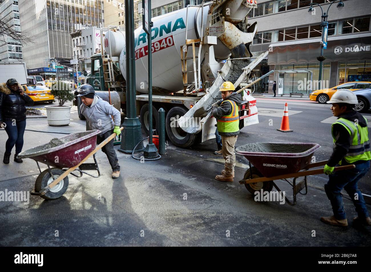 New York city Manhattan construction worker hand wheel barrow wet cement concrete on 3rd Av into a building Stock Photo