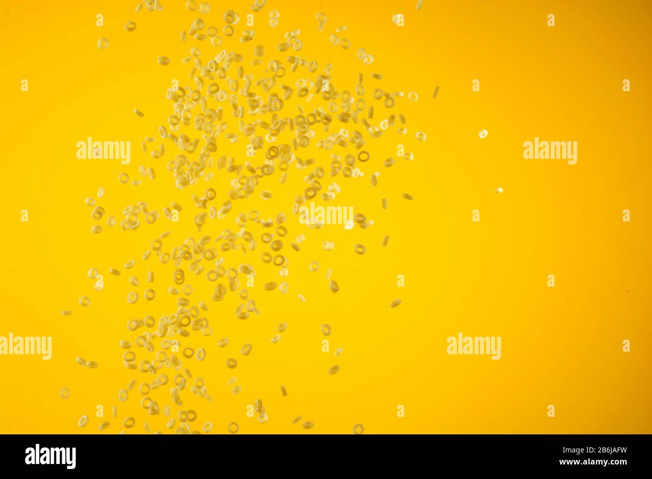 Concept of flying yellow raw italian pasta on yellow background with unfocused elements. Stock Photo