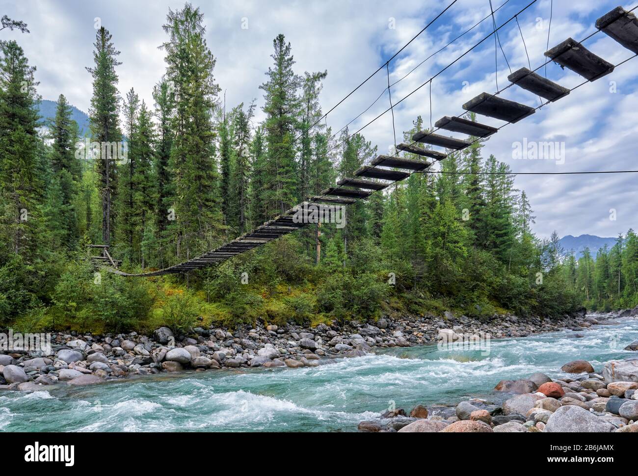 Pedestrian suspension bridge over a turbulent rivulet. Taiga of Eastern Siberia. Buryatia. Russia Stock Photo