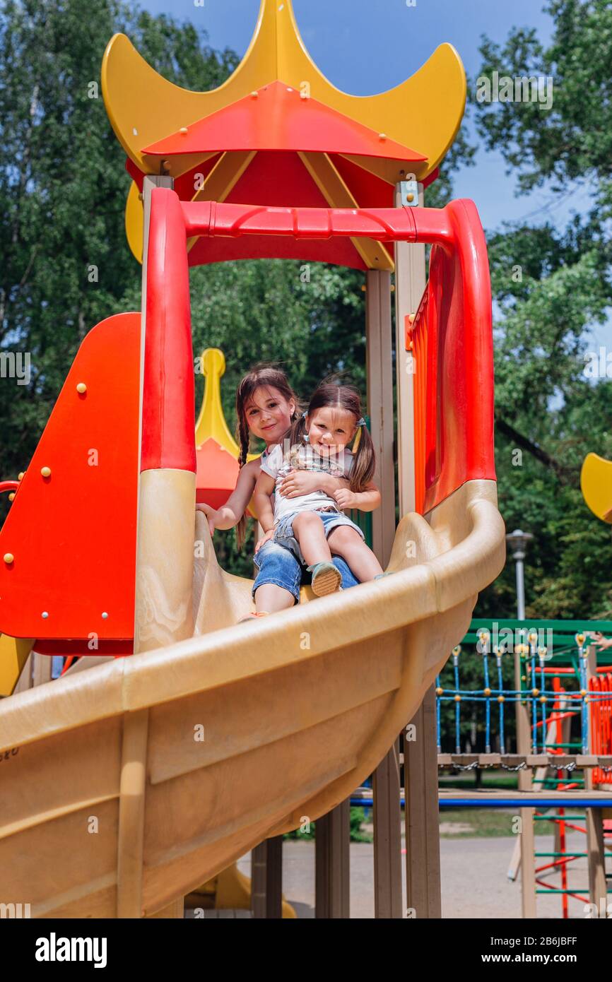 Two cute little girls having fun on a playground outdoors in summer ...