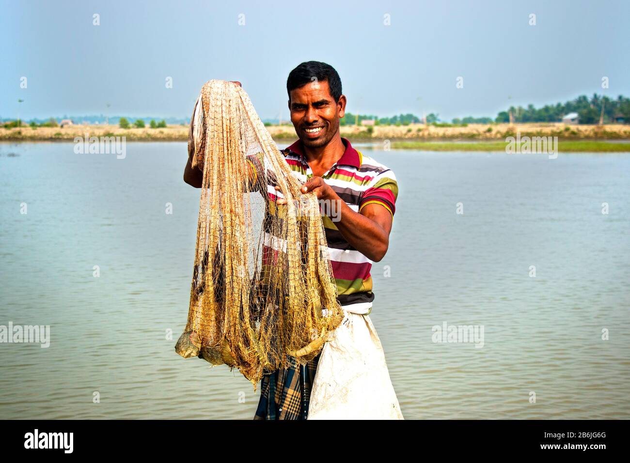 A fish farmer is showing his harvest with happy face. There are some shrimps in his net. Shrimp and prawn called white gold for Bangladeshi economy. Stock Photo