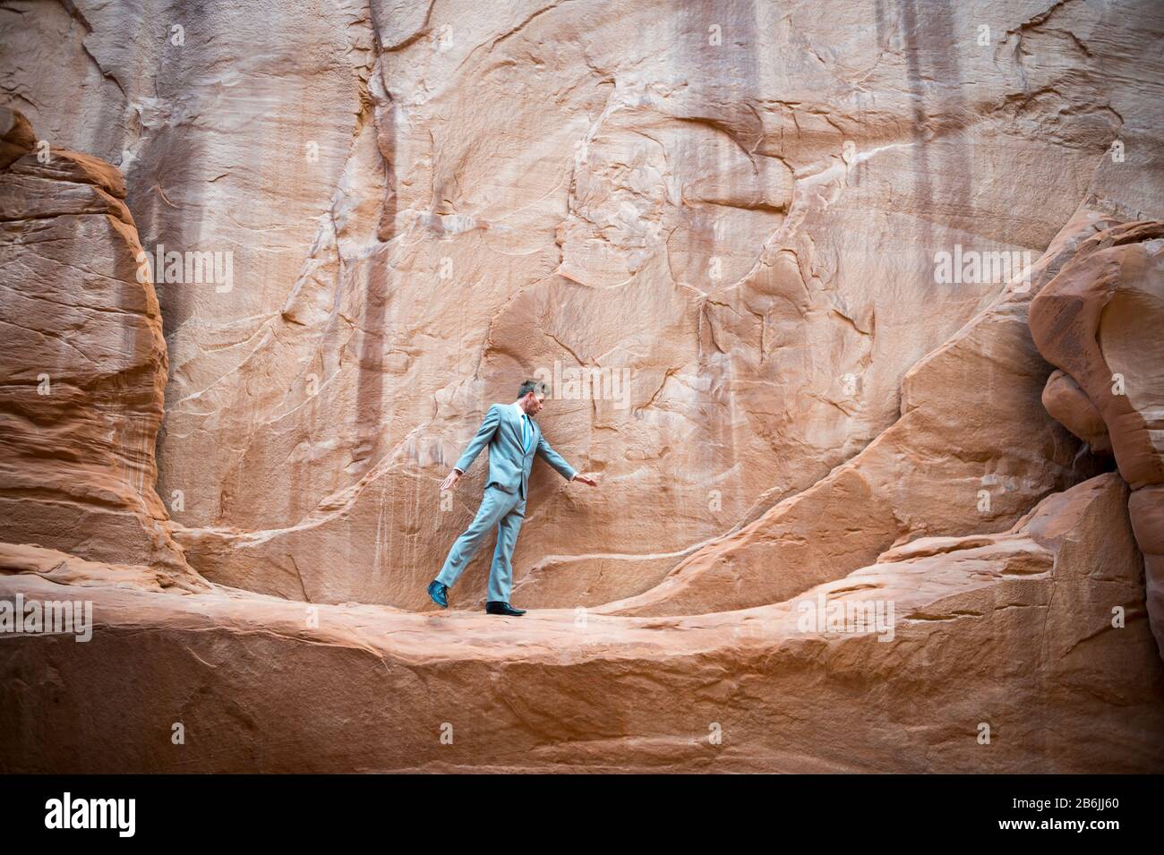 Nervous businessman taking a tentative step on a narrow ledge in a red rock canyon Stock Photo