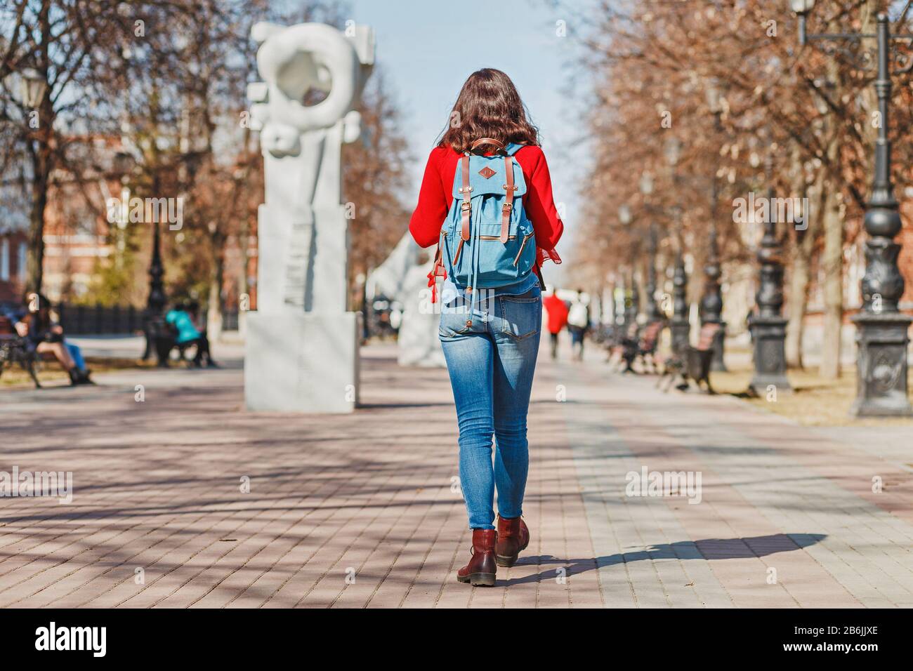 Hipster girl with backpack walking on a pedestrian street, rear view ...