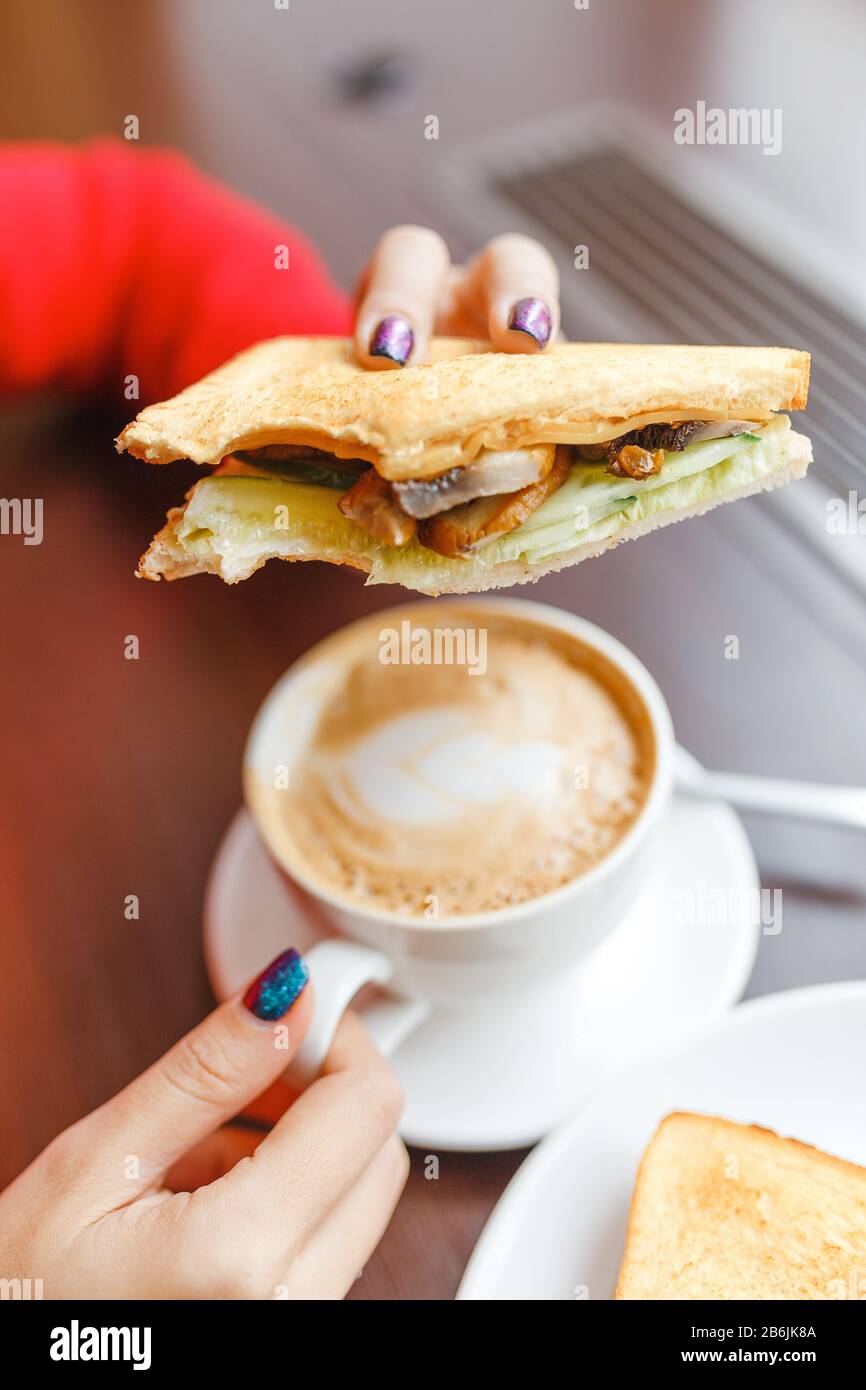 Hand holding Sandwich and coffee in white cup on the wooden table, cafe breakfast morning Stock Photo