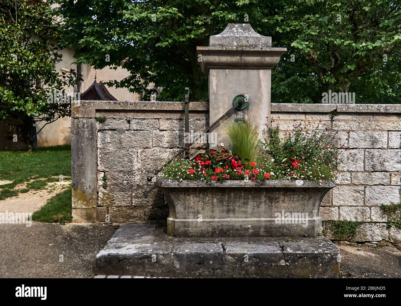 France, Ain departement, Auvergne - Rhone - Alpes région. The old stone water pump and its flowery trough on the church square in the Treffort medieval village hung on the first height of the Jura massif, Stock Photo