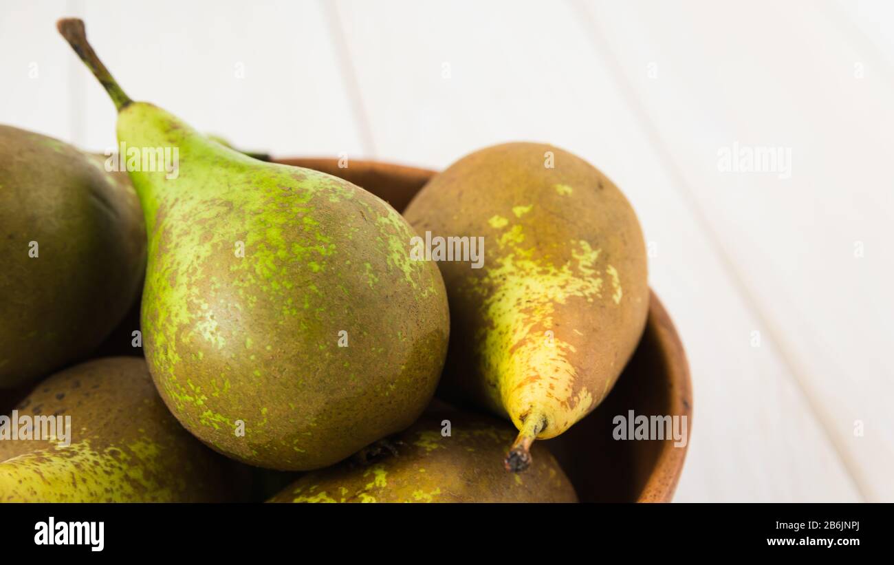 still life, green pears in a wooden plate on a white table, close-up Stock Photo