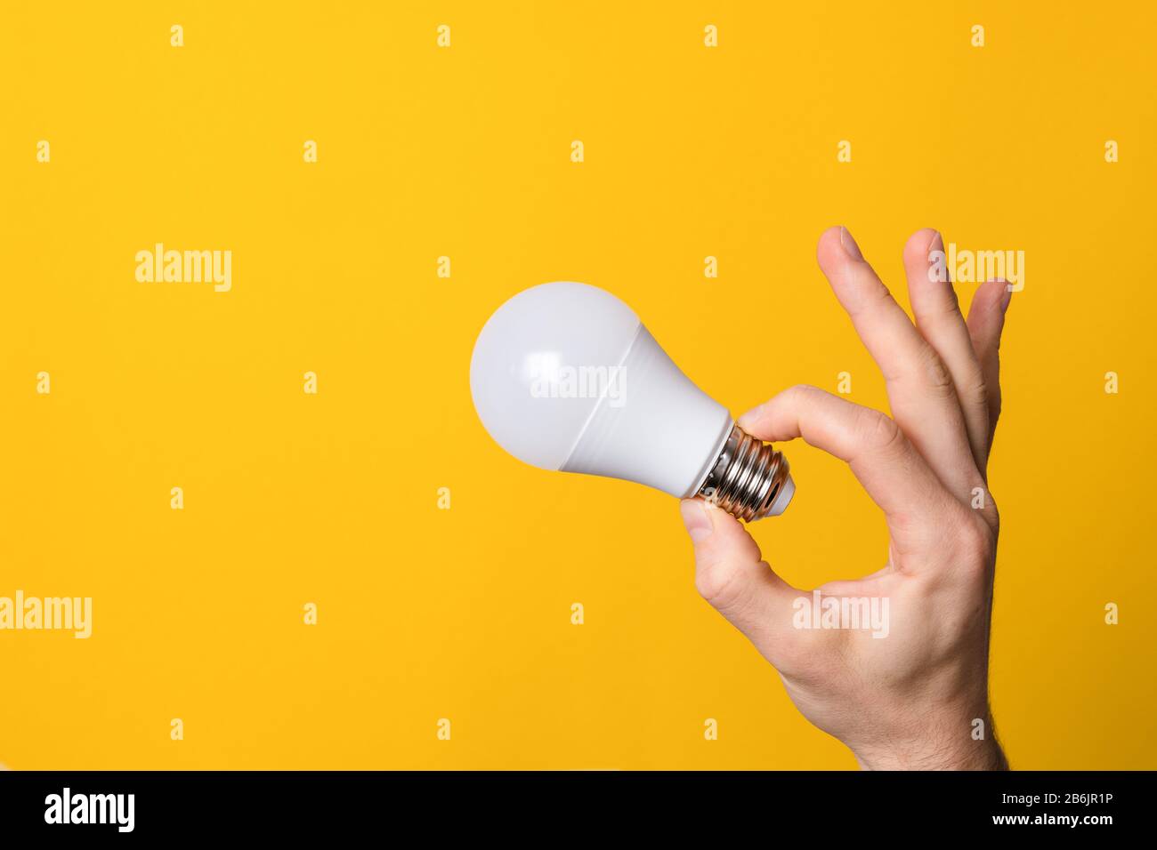 ok gesture closeup hand holding white led lighting bulb against a