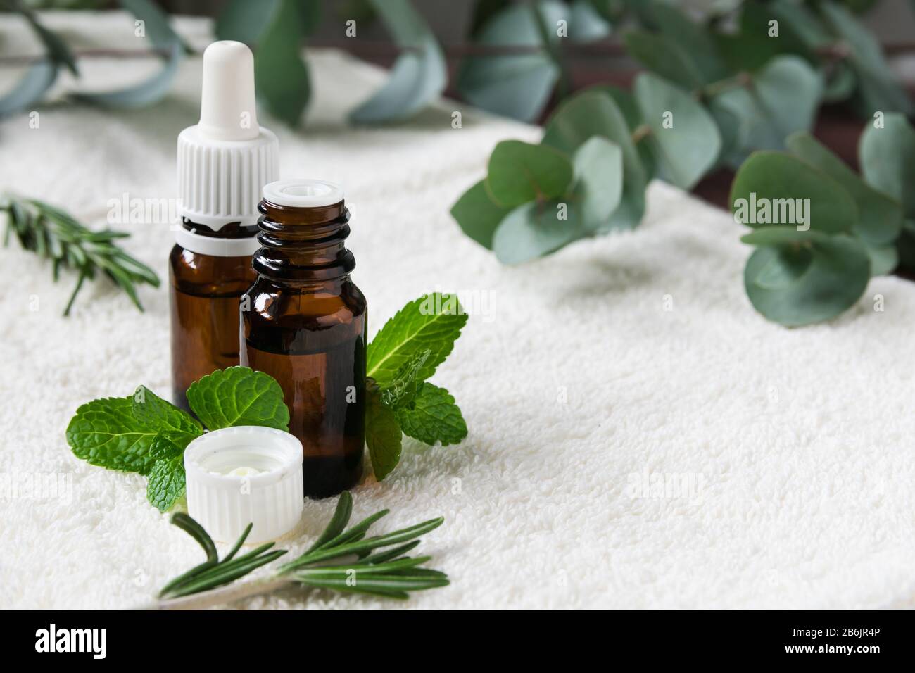 glass bottles with natural essential oils on a white towel with mint, rosemary and eucalyptus leaves Stock Photo