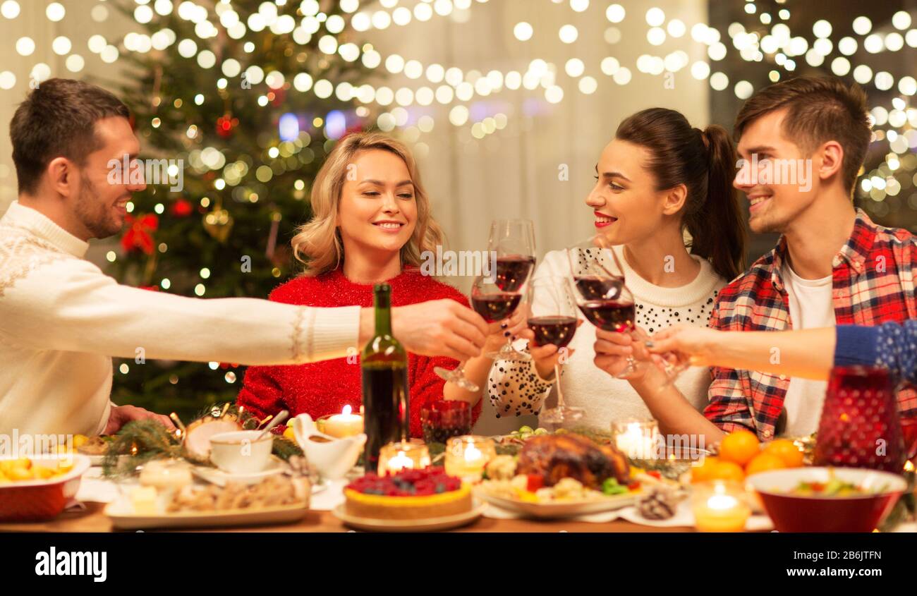 holidays and celebration concept happy friends having christmas dinner at home, drinking red
