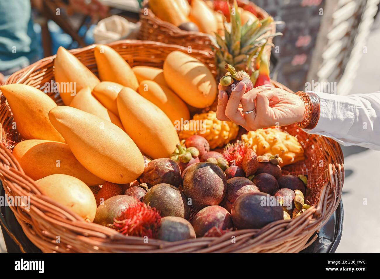 A young woman in a farmers' market chooses tropical exotic fruits rambutan, mango and dragon fruit Stock Photo