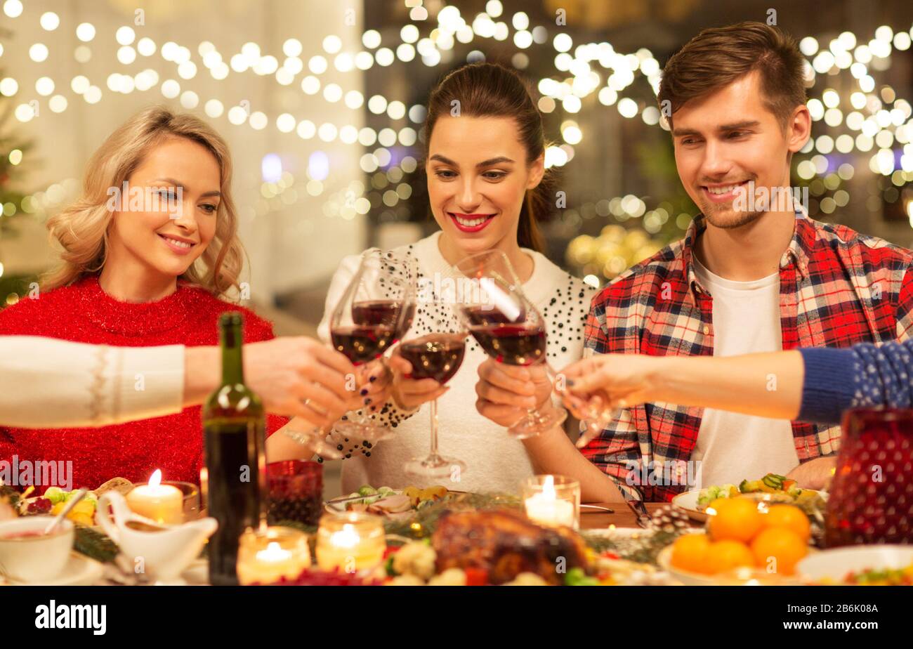 holidays and celebration concept happy friends having christmas dinner at home, drinking red
