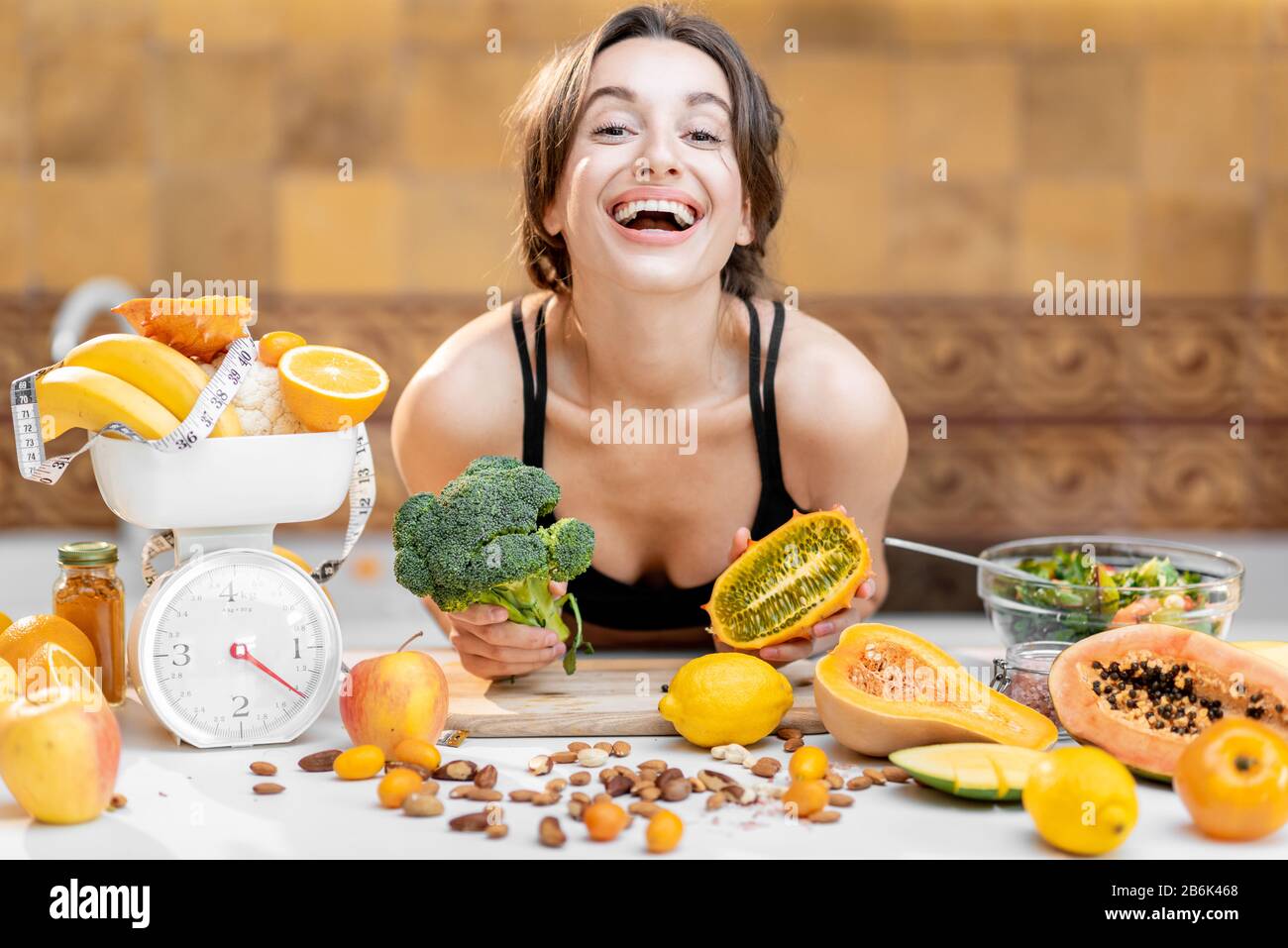 Portrait of a joyful sports woman with lots of healthy fresh food on the kitchen. Concept of losing weight, sports and healthy eating Stock Photo
