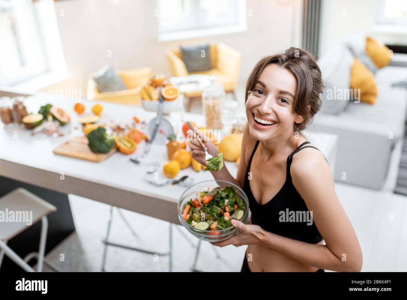 Portrait of a cheerful athletic woman eating healthy salad during a break at home. Concept of losing weight, sports and healthy eating Stock Photo