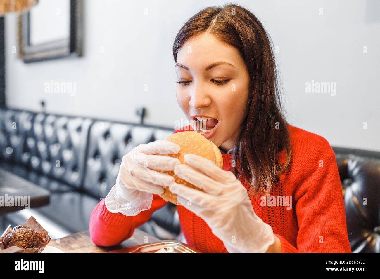 Woman's hands in gloves holding burger in modern fastfood restaurant Stock Photo