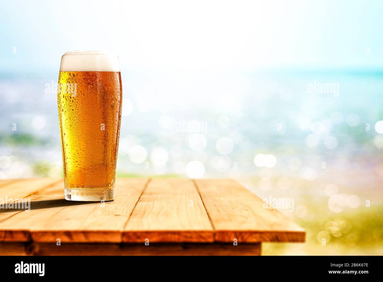 Cold beer in big glass on wooden table with ocean and sandy beach  background. Copy space for advertising product Stock Photo - Alamy